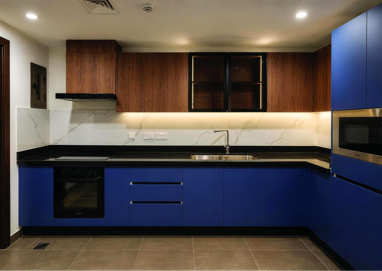 Kitchen with blue lower cabinets, wood upper cabinets, marble-effect splashback and built-in oven